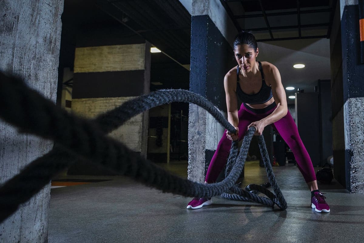 A woman working battle ropes in a gym with concrete pillars