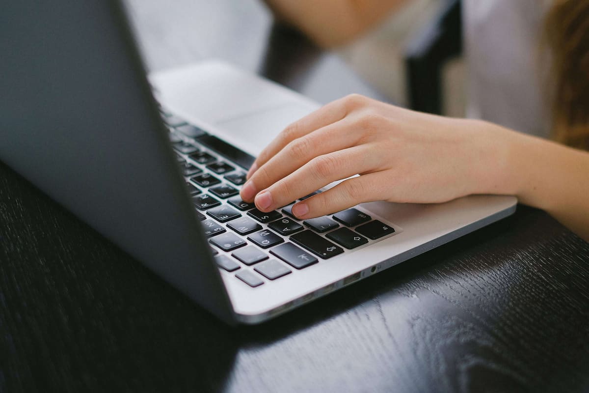 A hand typing on a laptop keyboard on a dark wooden desk