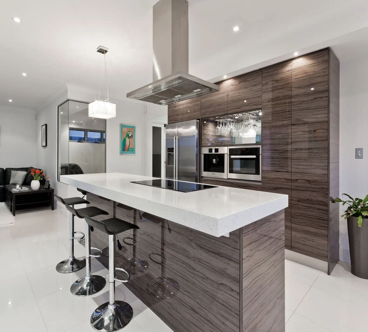 A modern kitchen with a white island, black bar stools, wood-grain cabinets and a steel range hood